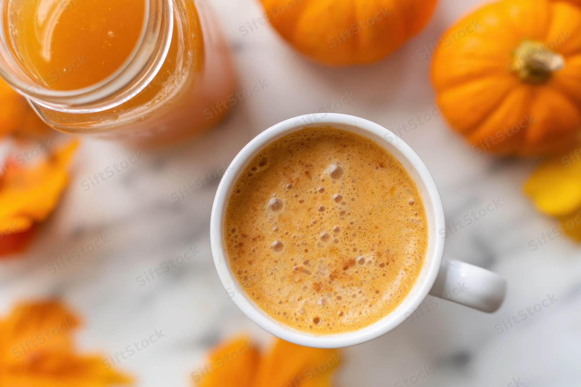 Frothy pumpkin coffee in a white mug on a marble table surrounded by pumpkins and autumn leaves