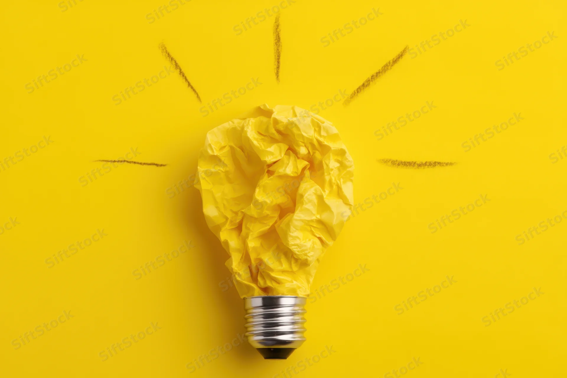 Crumpled yellow paper shaped like a lightbulb with drawn rays on a yellow background