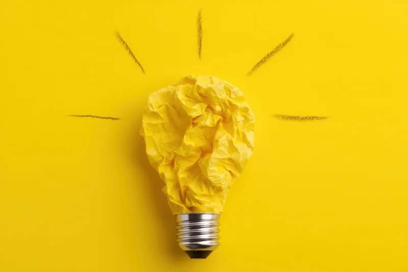 Crumpled yellow paper shaped like a lightbulb with drawn rays on a yellow background