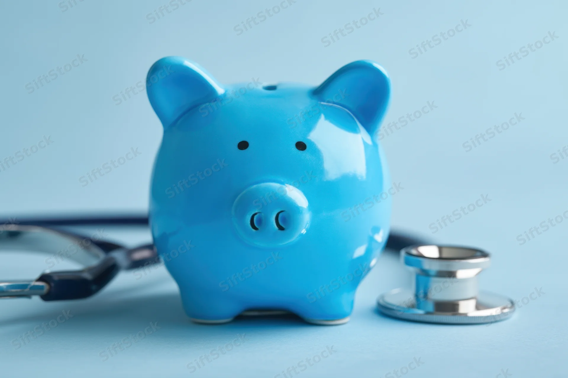 Blue piggy bank with stethoscope on light blue surface