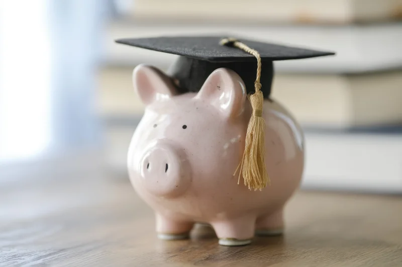 Pink ceramic piggy bank wearing black graduation cap with gold tassel on wooden table