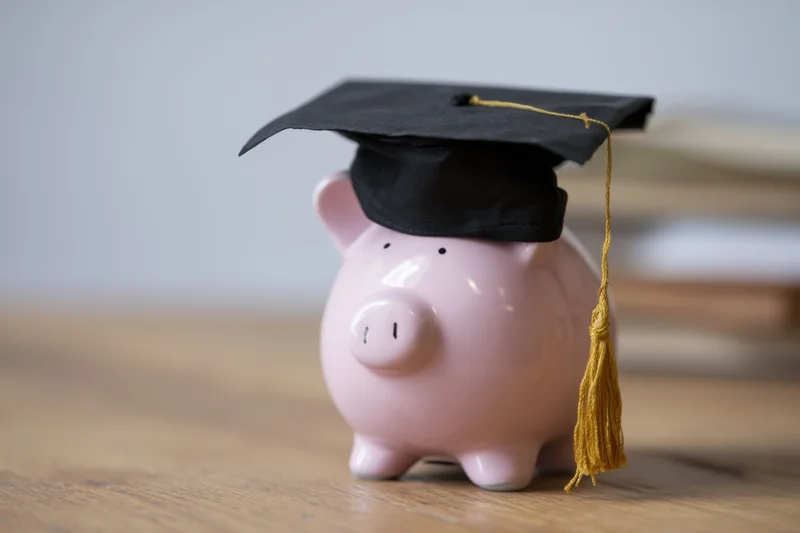 Pink ceramic piggy bank wearing black graduation cap with gold tassel on wooden table