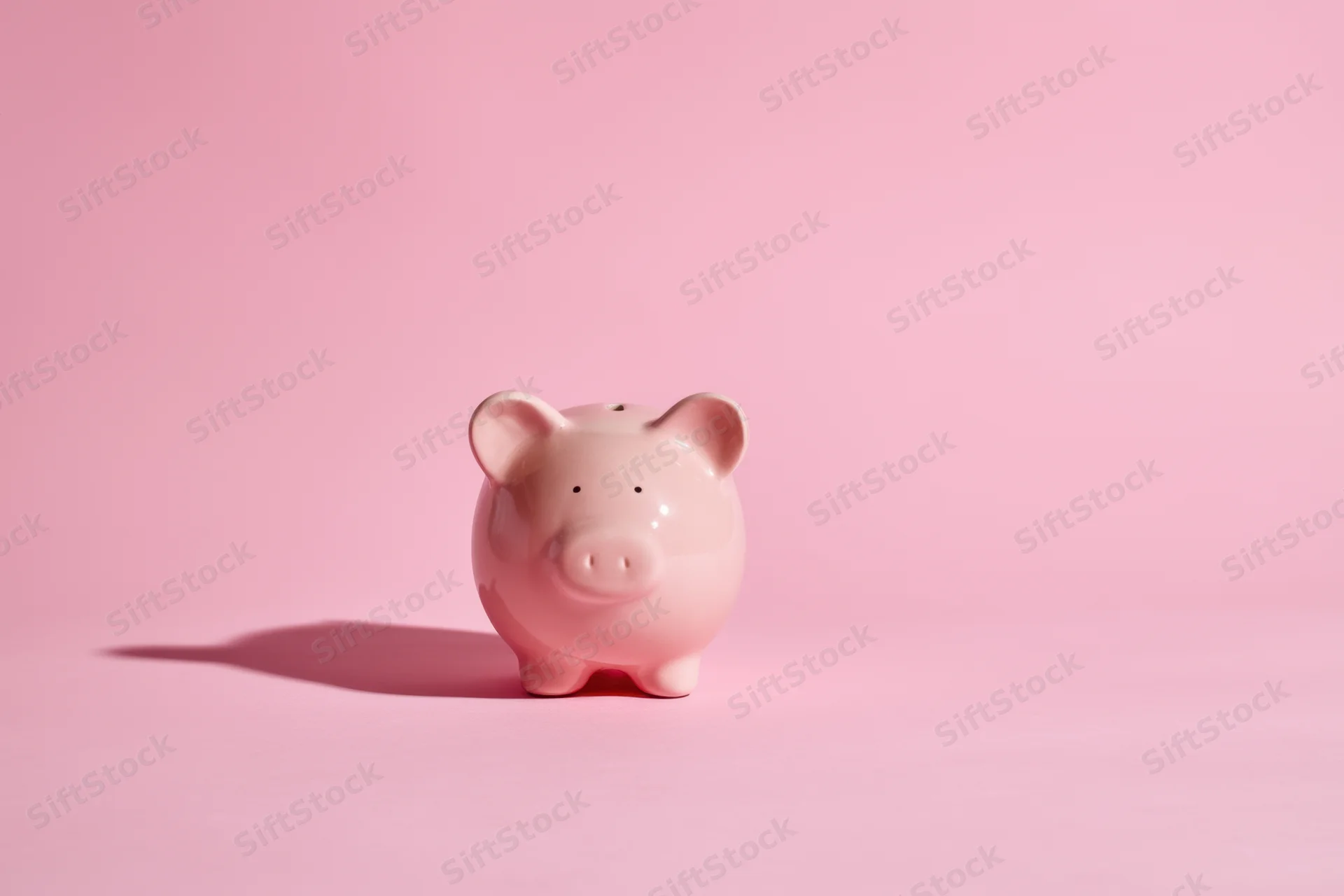 Pink ceramic piggy bank standing on a soft pink surface with shadow cast to the left