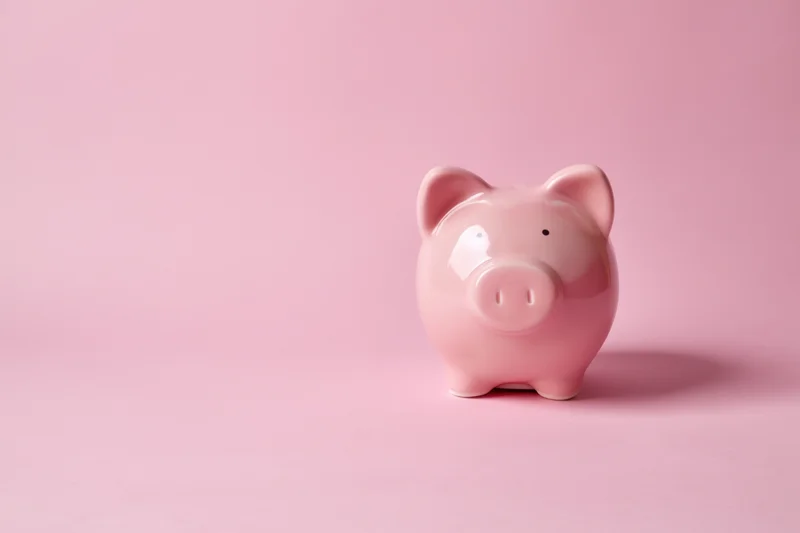 Pink ceramic piggy bank standing on a soft pink surface with copyspace to the left