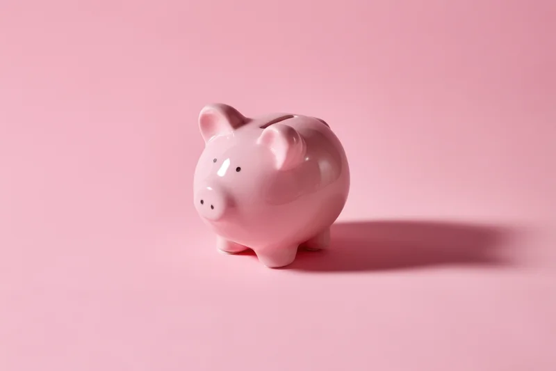 Pink ceramic piggy bank standing on soft pink surface with shadow cast to the right