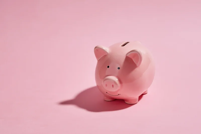 Pink ceramic piggy bank with coin slot on soft pink background casting shadow