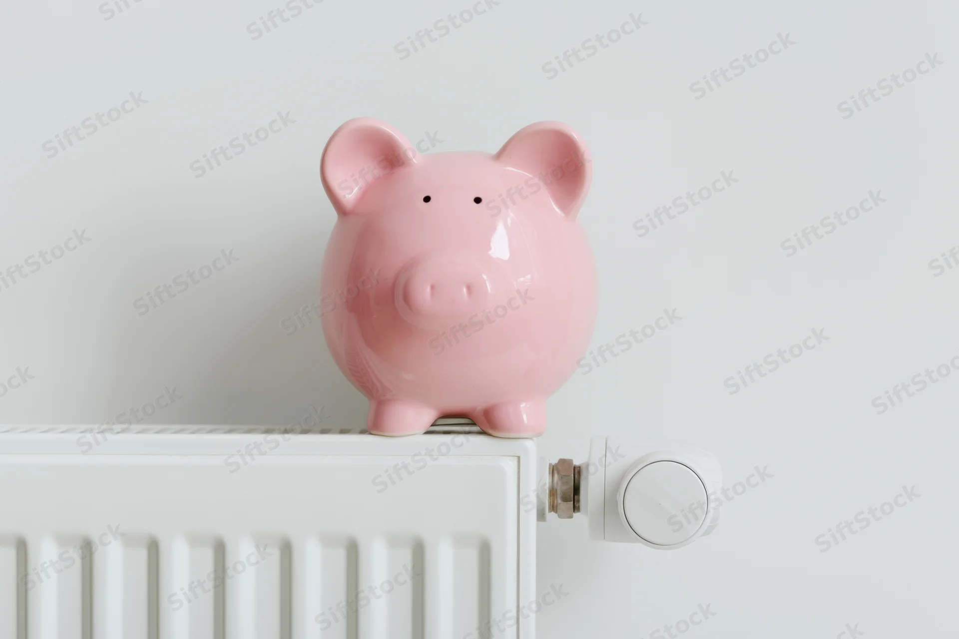 Pink ceramic piggy bank sitting on top of white radiator in indoor home setting