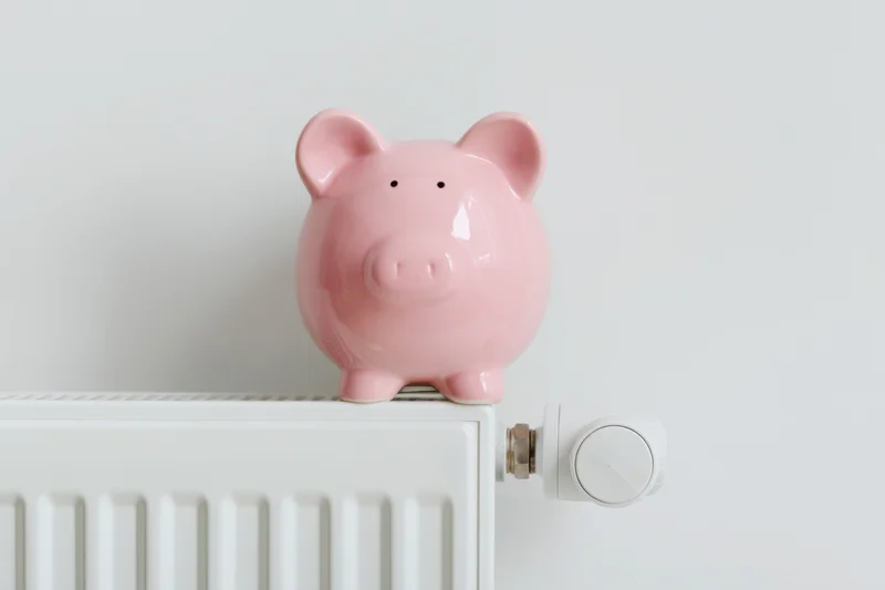 Pink ceramic piggy bank sitting on top of white radiator in indoor home setting