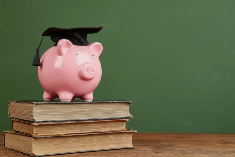 Pink piggy bank wearing graduation cap on stack of books on wooden table against green background