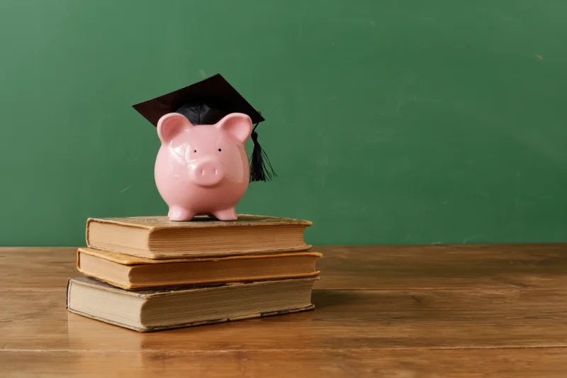 Pink piggy bank wearing graduation cap on stack of books on wooden table in front of green chalkboard