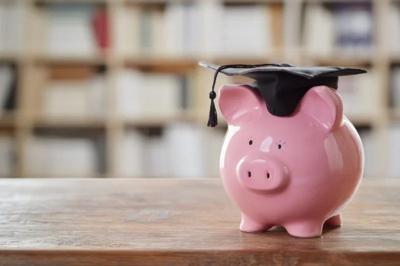 Pink piggy bank wearing graduation cap on wooden desk with bookshelf in background