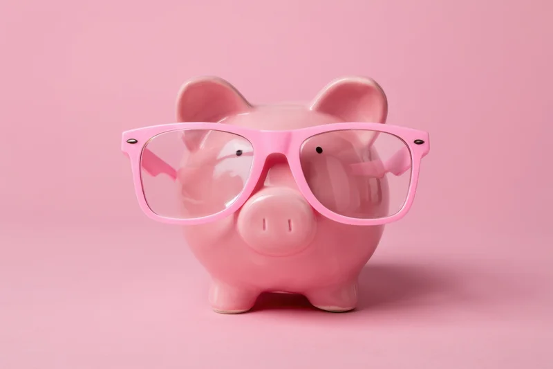 Pink piggy bank wearing oversized pink glasses on a solid pink background