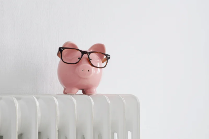 Pink piggy bank wearing glasses perched on white radiator in minimalist interior