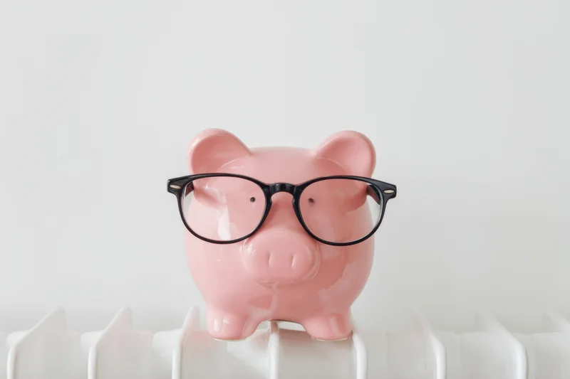 Pink ceramic piggy bank wearing black glasses perched on white ridged surface against plain background
