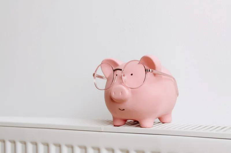 Pink piggy bank wearing round glasses perched on a white shelf above a radiator