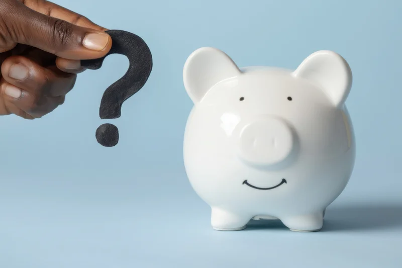 White ceramic piggy bank with smiling face beside a hand holding a black question mark against a blue background