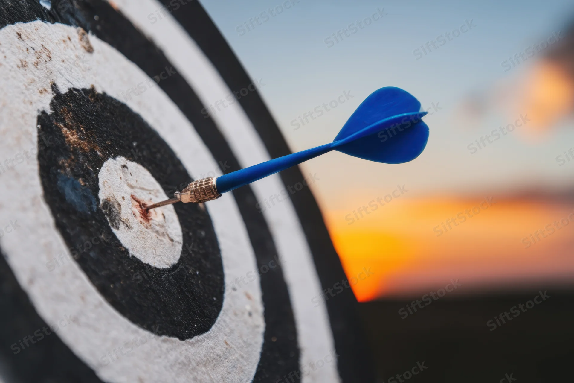 Blue dart striking the center of a bullseye on a target at sunset