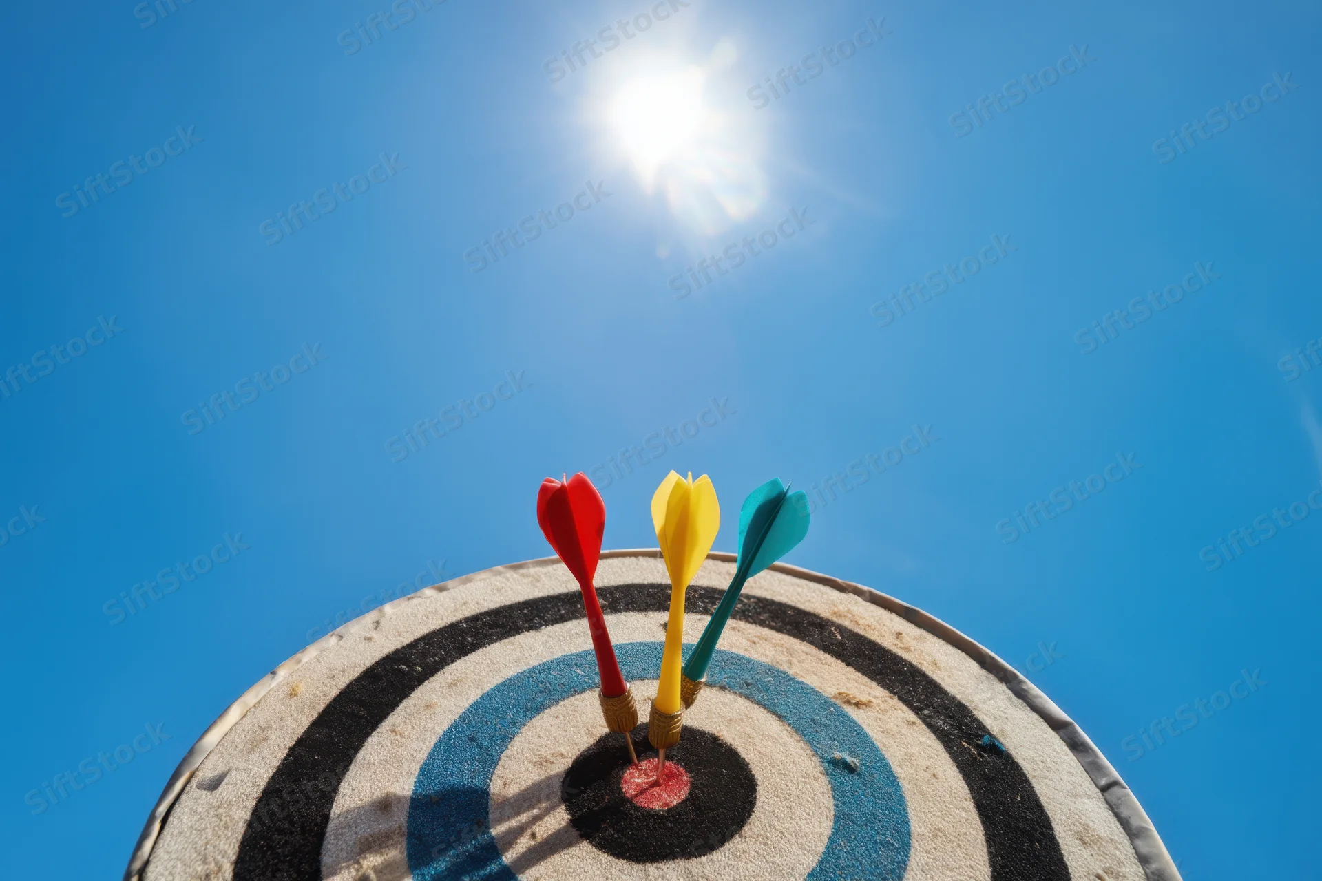 Dartboard with three colorful darts hitting the bullseye against a bright blue sky