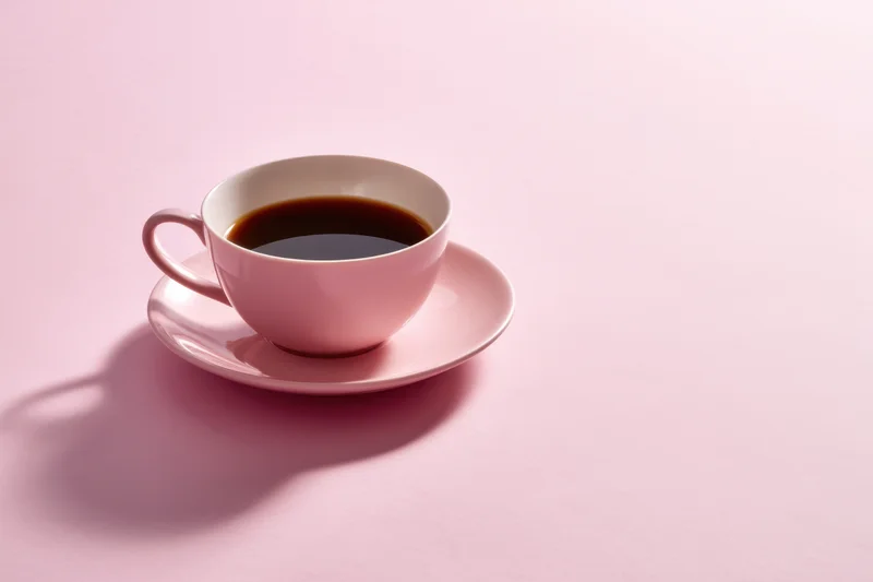 Pink ceramic cup with dark coffee on matching saucer on a plain pink surface