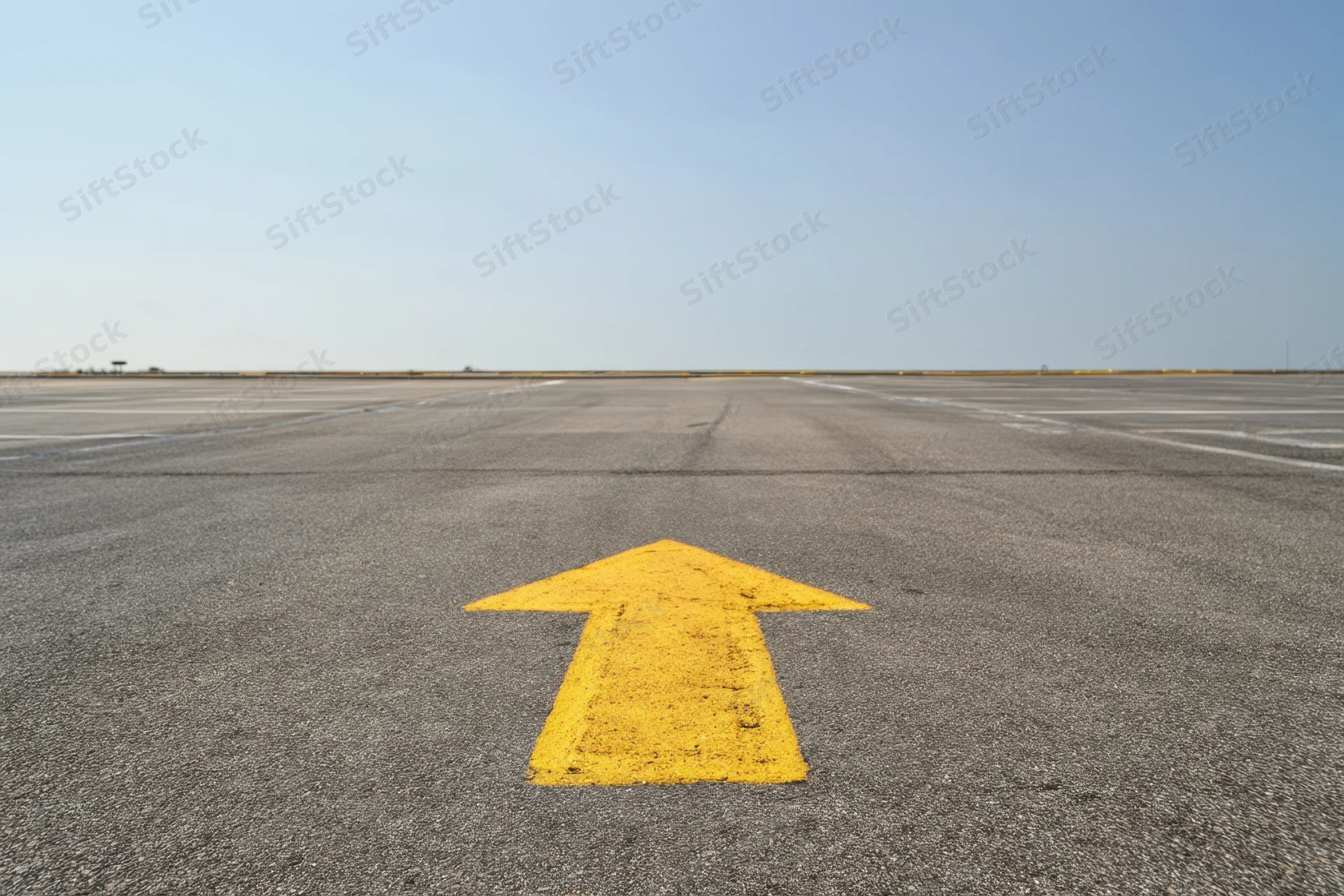 Yellow arrow painted on airport tarmac pointing straight ahead toward horizon