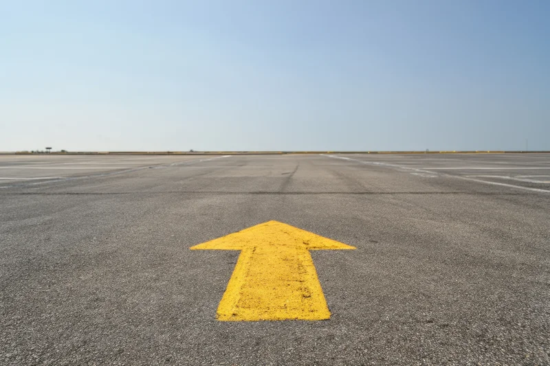 Yellow arrow painted on airport tarmac pointing straight ahead toward horizon