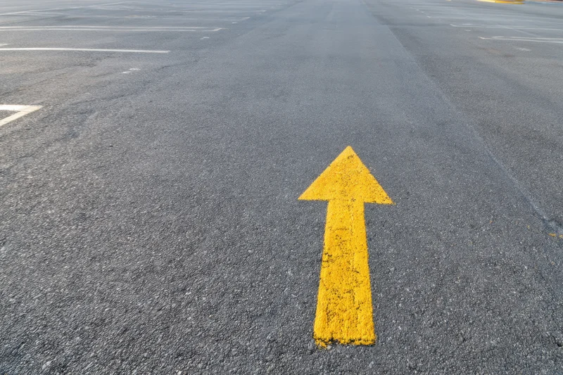 Yellow arrow painted on asphalt parking lot surface pointing forward
