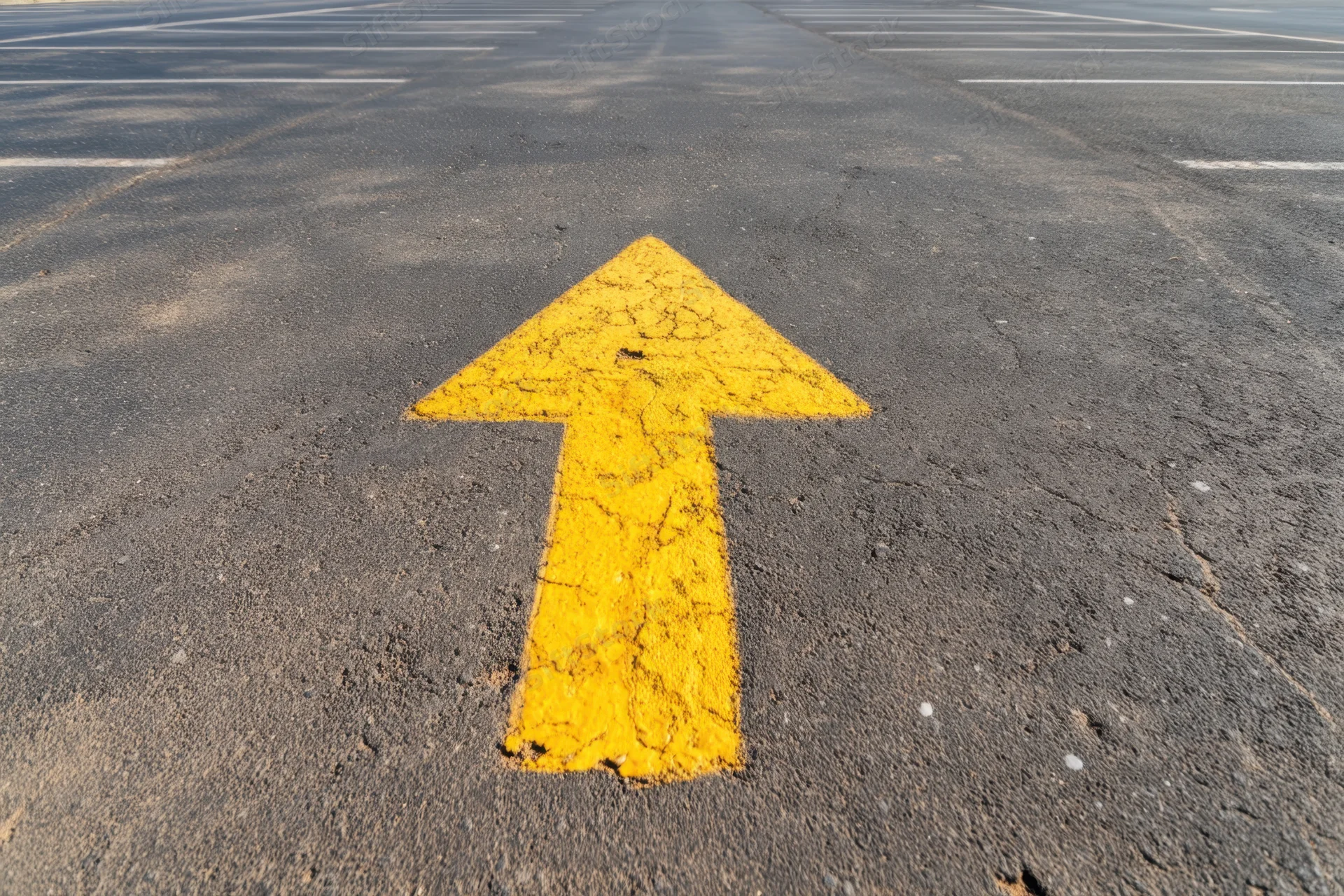 Yellow arrow painted on asphalt parking lot surface pointing forward