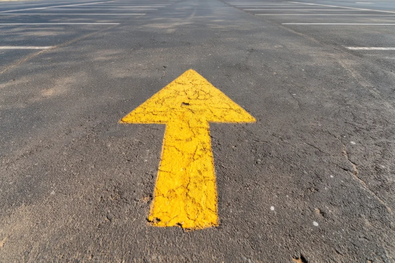 Yellow arrow painted on asphalt parking lot surface pointing forward