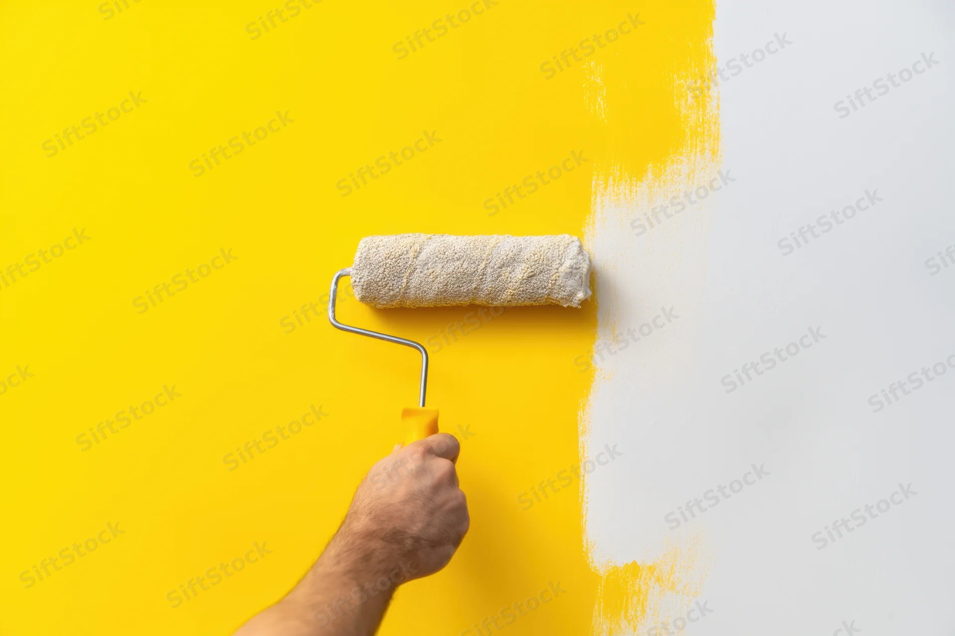 Hand holding paint roller applying white paint to a yellow wall during home renovation