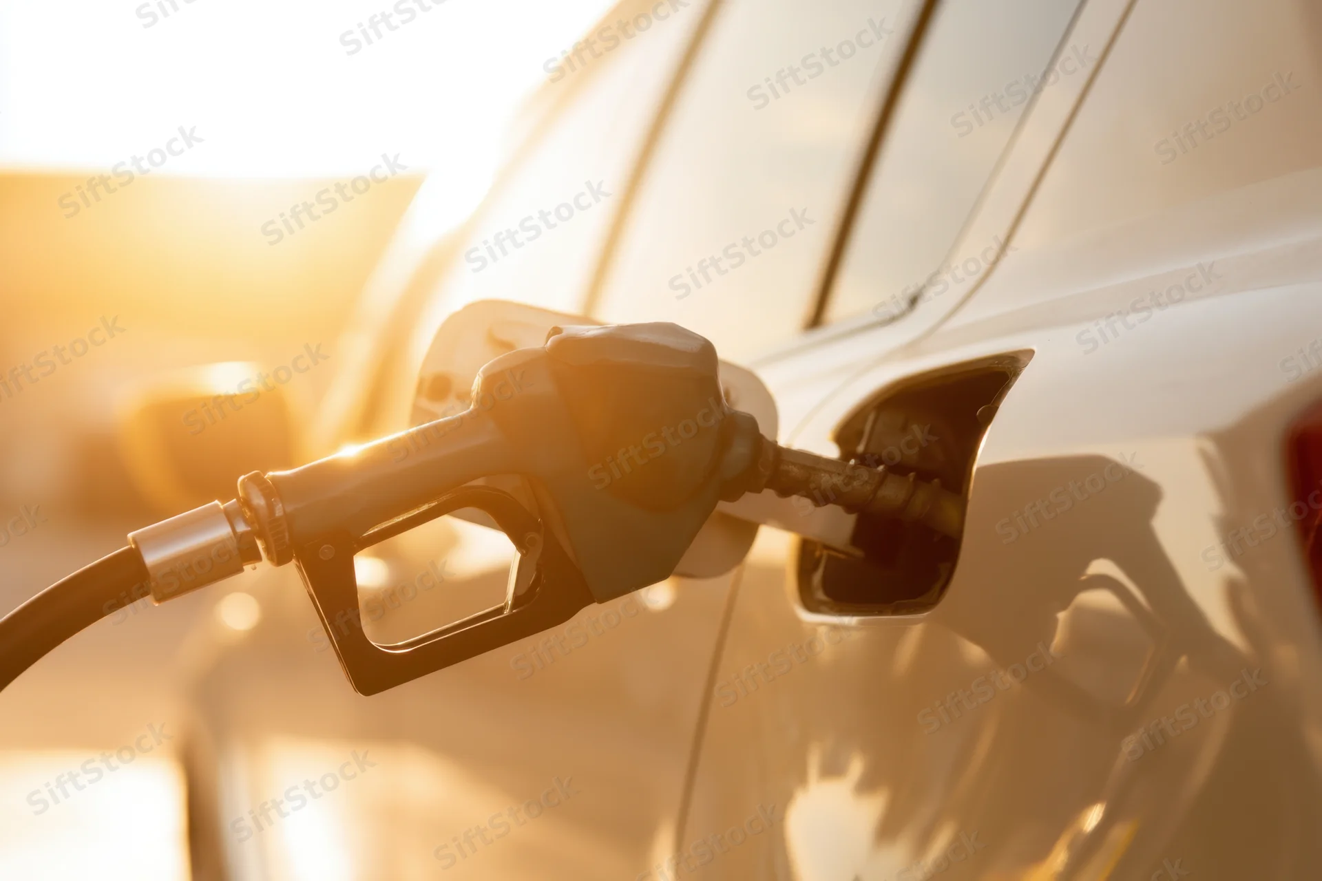Fuel nozzle inserted into car gas tank during golden hour sunlight