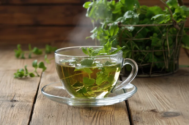 Steaming mint tea in a glass cup with fresh leaves garnish on a wooden table
