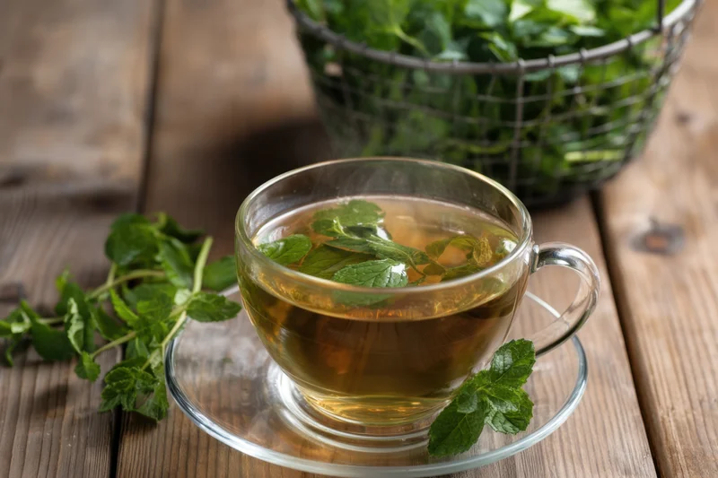 Glass cup of steaming mint tea with fresh mint leaves on wooden table