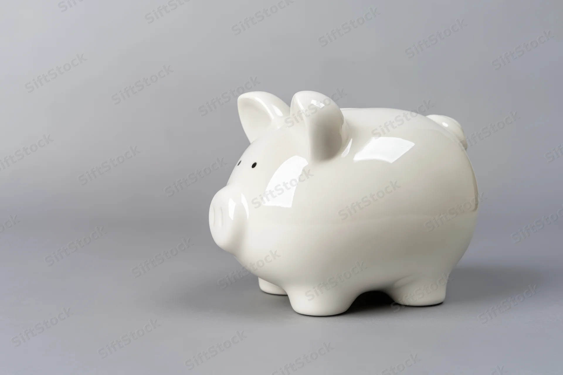 Glossy white ceramic piggy bank sitting on a plain grey surface