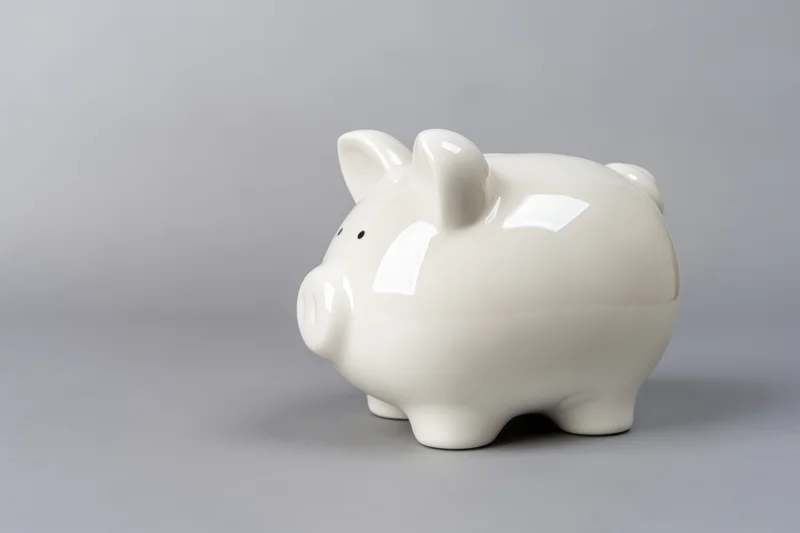 Glossy white ceramic piggy bank sitting on a plain grey surface