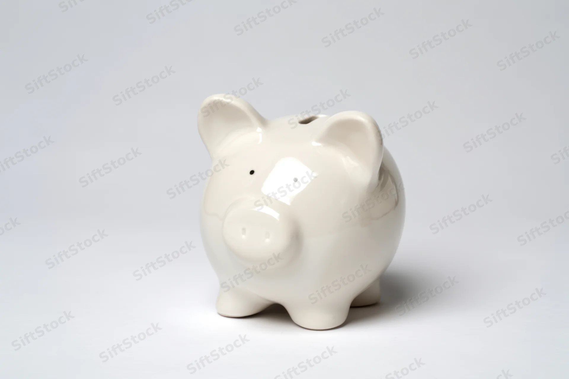 Glossy white ceramic piggy bank sitting on a plain grey surface