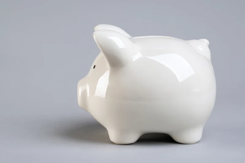 Glossy white ceramic piggy bank sitting on a plain grey surface