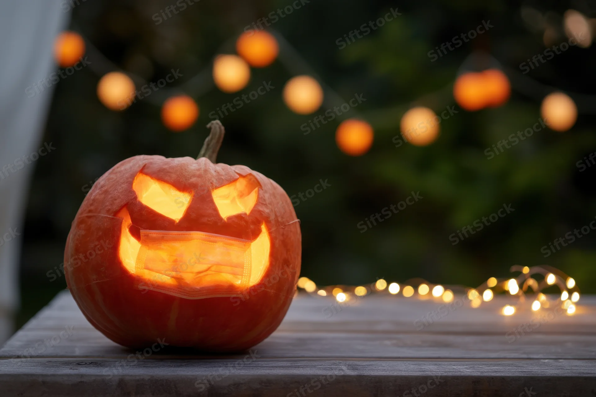 Carved pumpkin with face mask glowing on wooden table outdoors at night