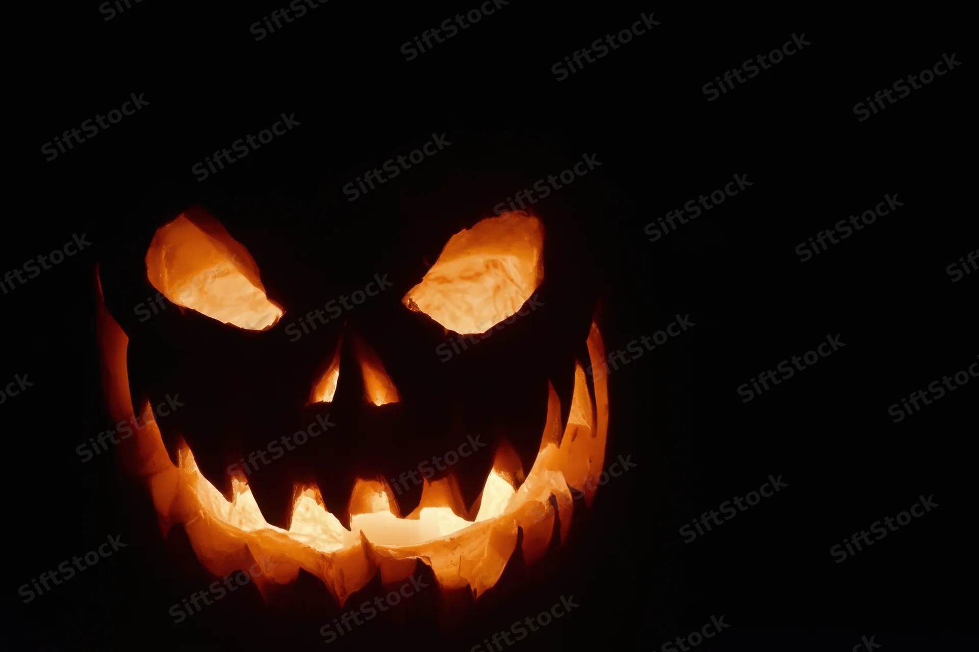 Glowing carved pumpkin with jagged grin against black background