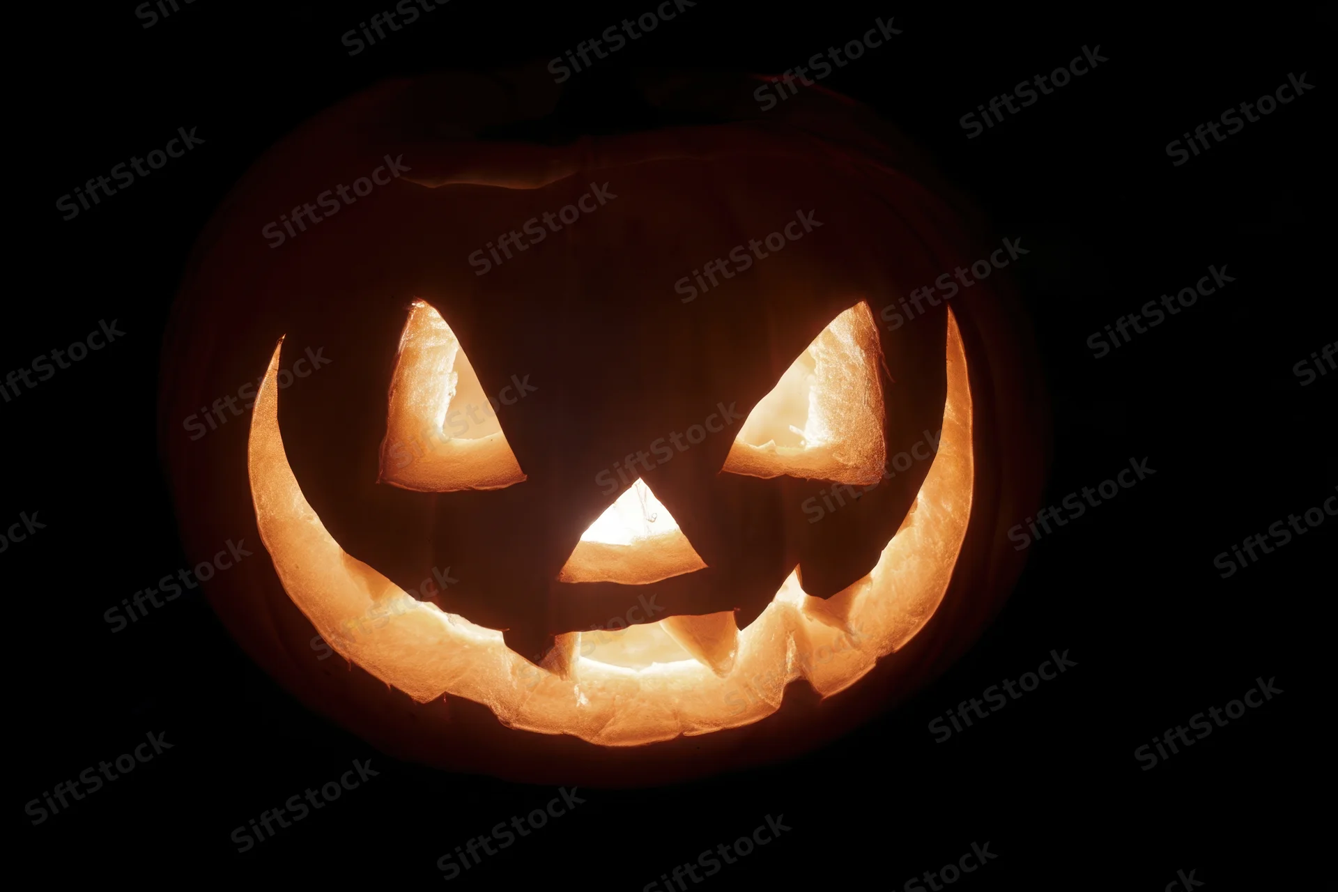 Glowing carved pumpkin with triangular eyes and wide grin against black background