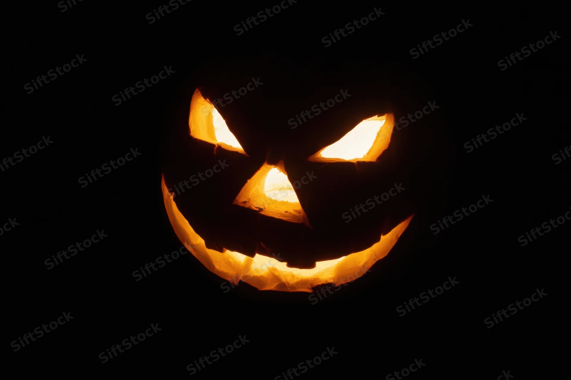 Glowing carved pumpkin with triangular eyes and jagged smile against black background