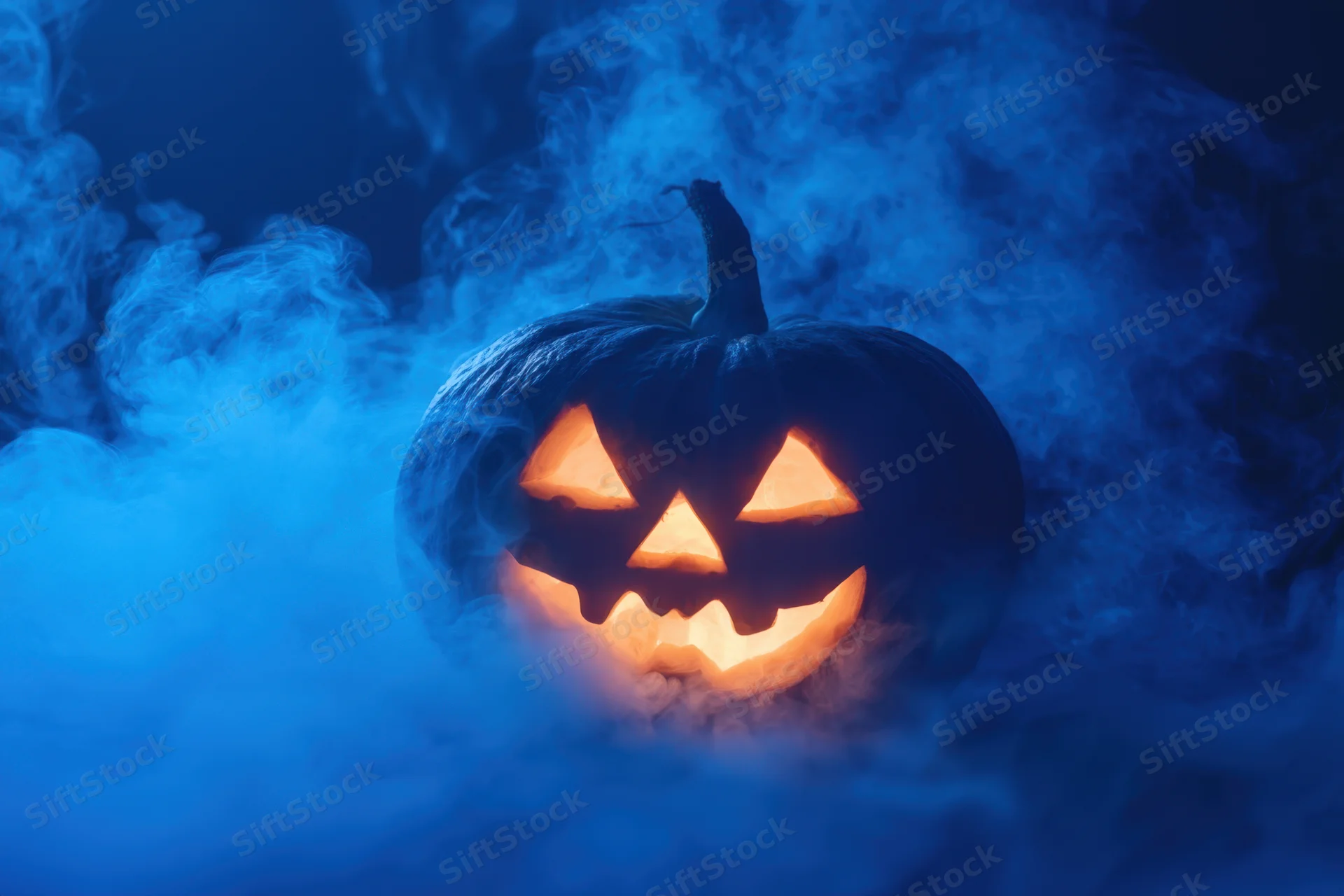 Glowing jack-o-lantern with carved face surrounded by swirling blue mist at night
