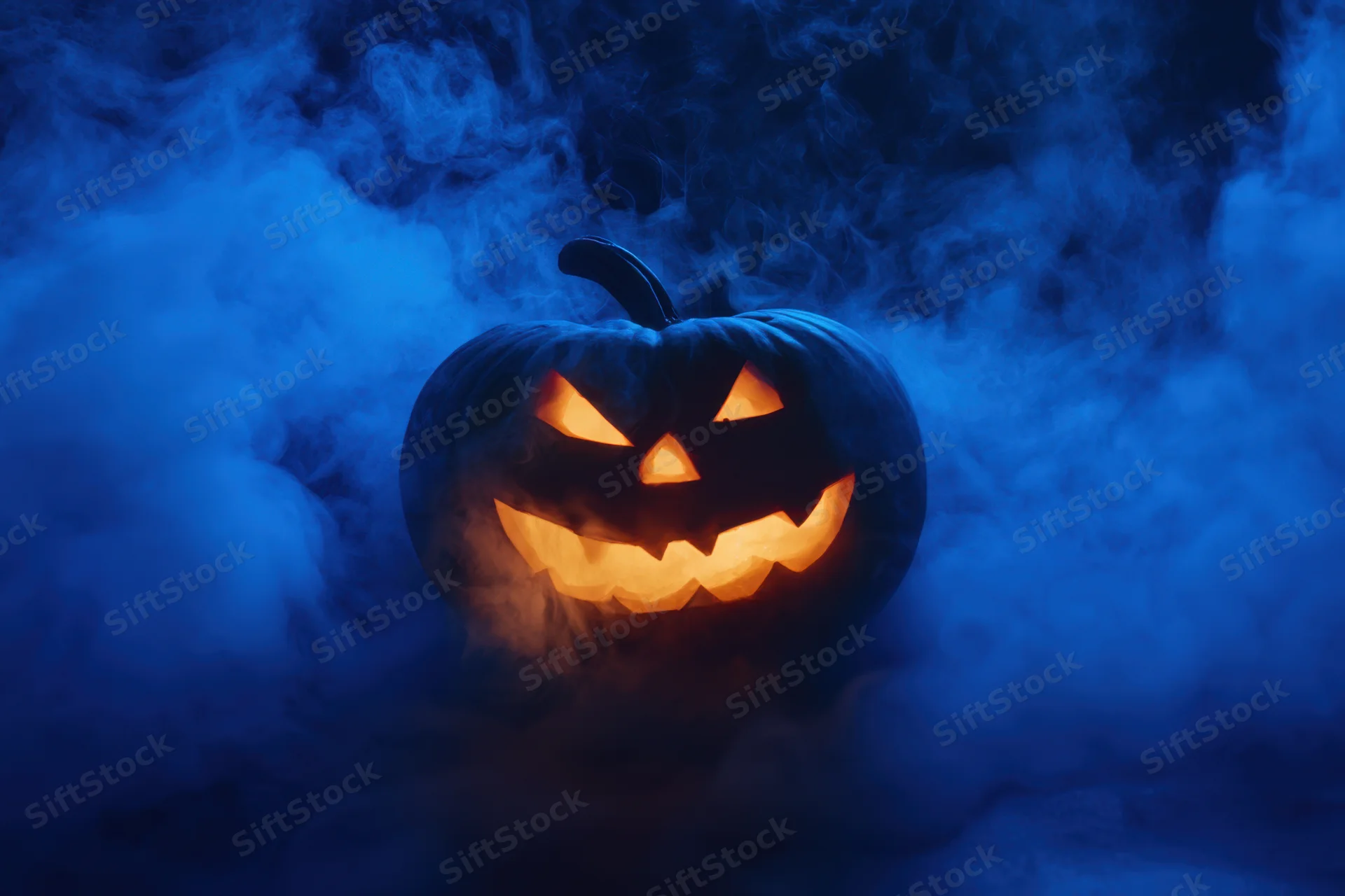 Glowing carved pumpkin with jagged face surrounded by swirling blue mist at night
