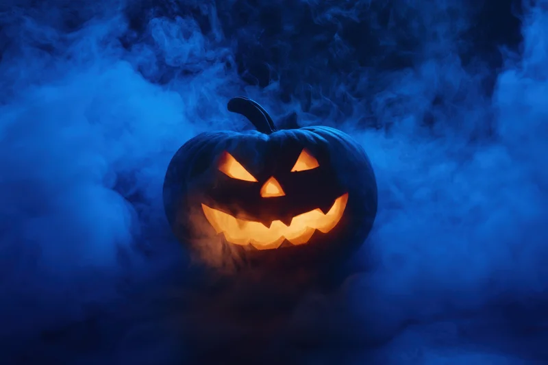 Glowing carved pumpkin with jagged face surrounded by swirling blue mist at night