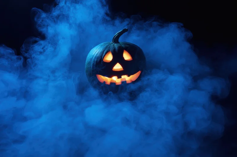 Glowing jack-o-lantern with carved face surrounded by swirling blue mist at night