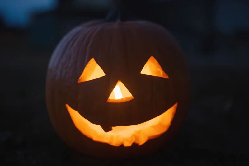 Glowing jack-o-lantern with carved triangular eyes and wide grin lit from within at night outdoors