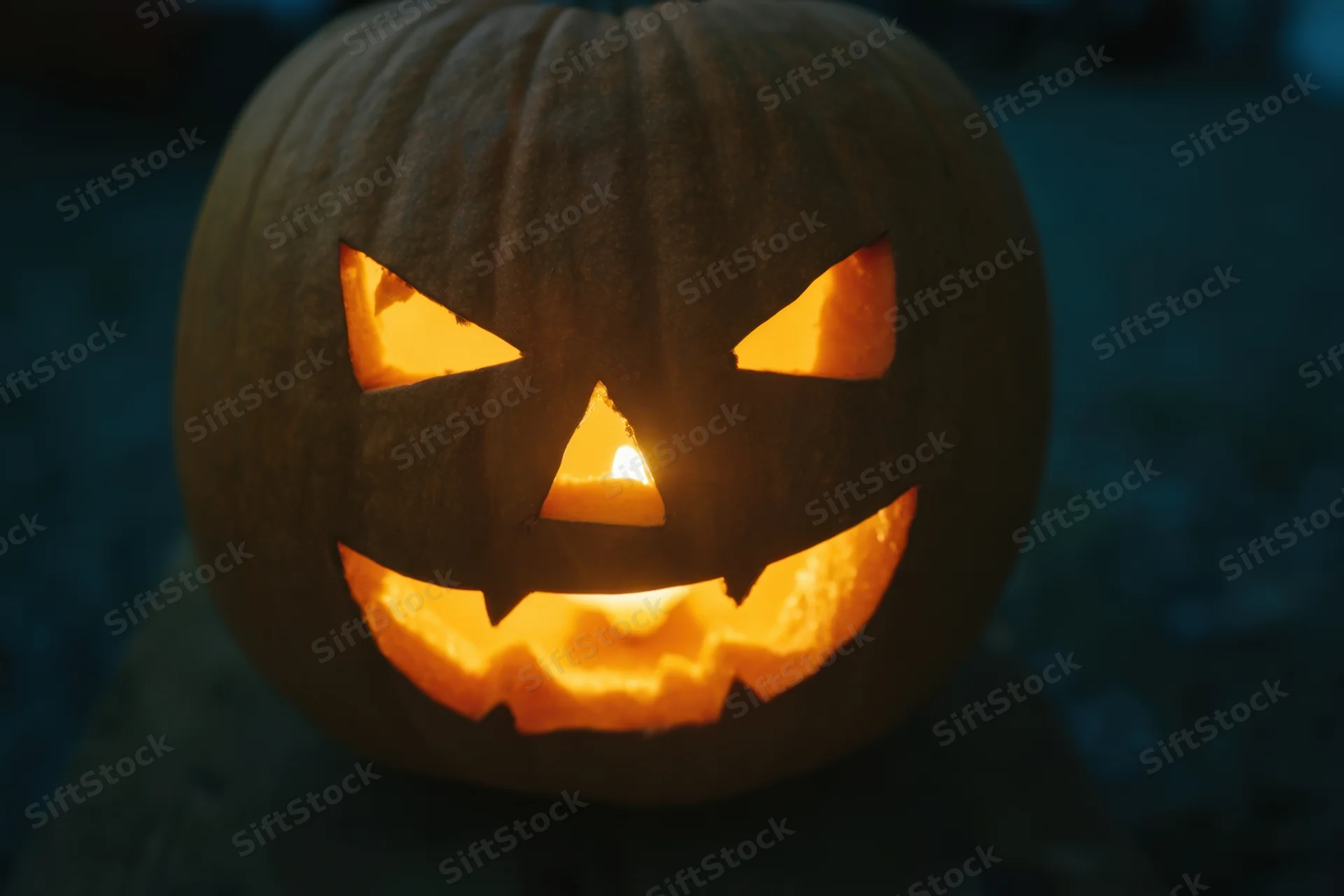 Glowing jack-o-lantern with carved menacing grin lit from within at night