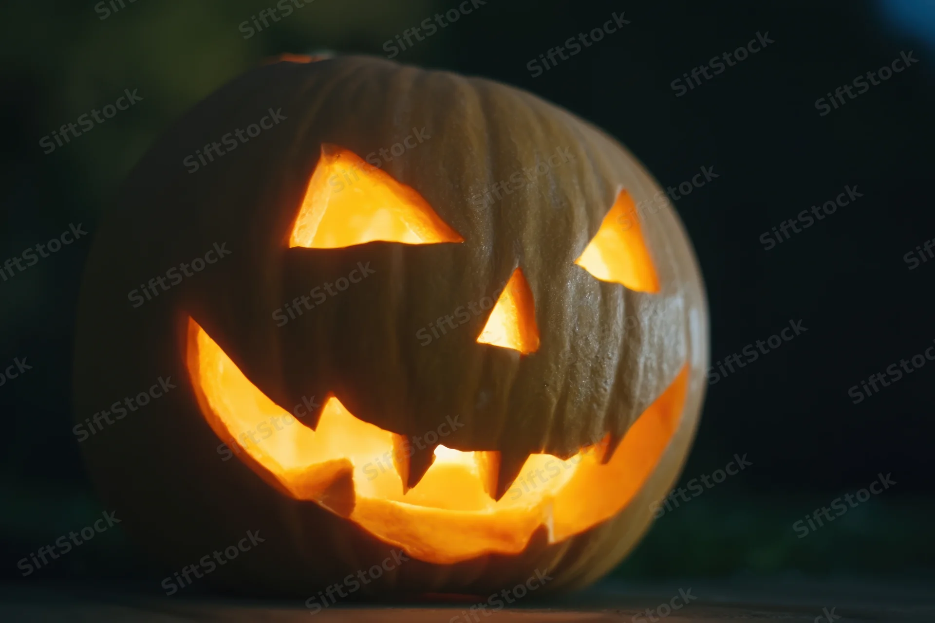 Glowing jack-o-lantern with carved menacing grin lit from within at night
