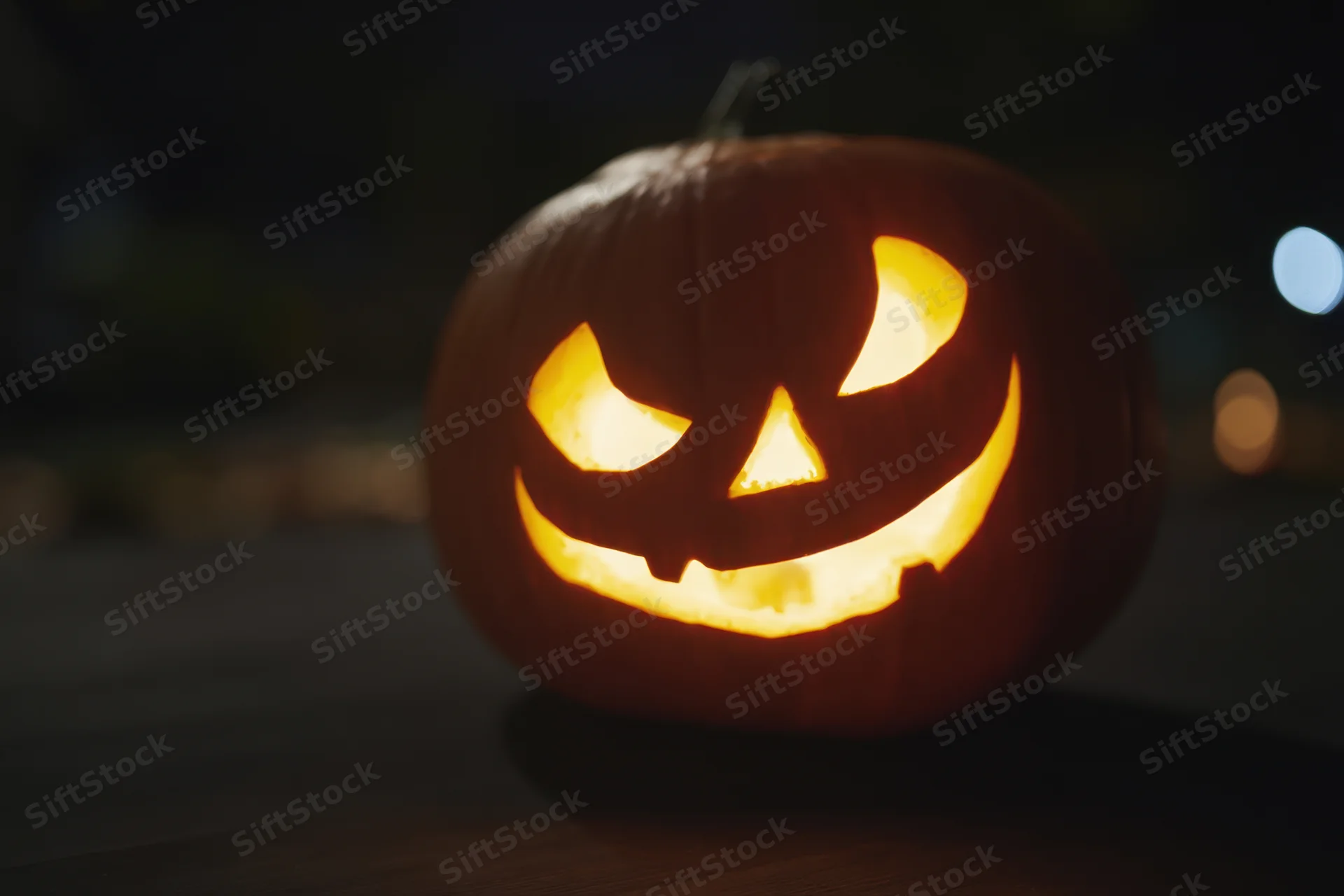 Glowing jack-o-lantern with mischievous carved face on wooden surface at night