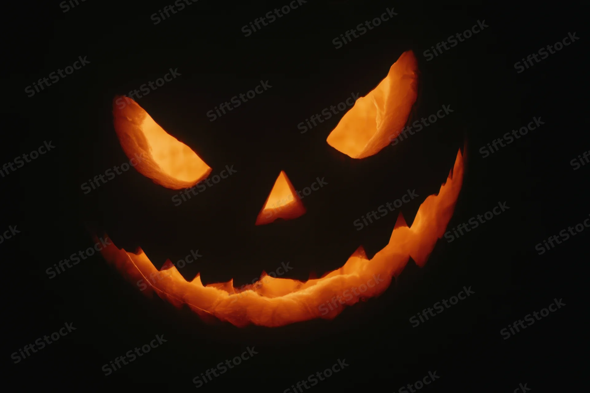 Glowing jack-o-lantern with carved face and eerie grin in darkness