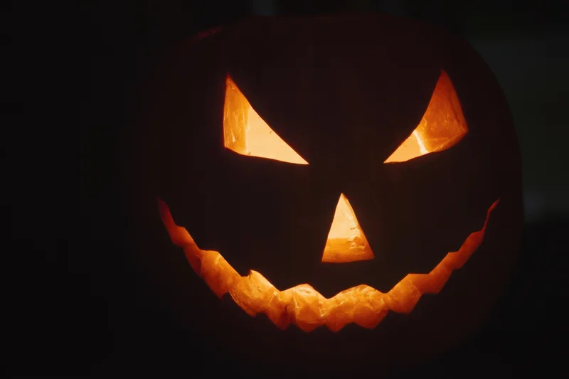 Glowing jack-o-lantern with carved triangular eyes nose and jagged grin in dark setting